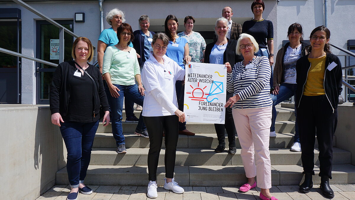 Teilnehmerinnen und Teilnehmer der Fachgruppe Qualitätskriterien stehen auf der Treppe vor dem Mehrgenerationenhaus Weidenbach