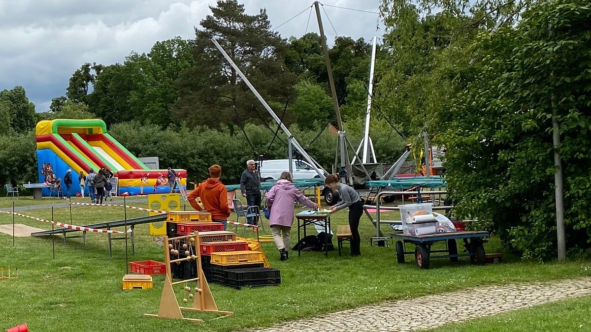 Auf einer Wiese stehen ein Trampolin, eine aufblasbare Rutsche und weitere Spielutensilien.