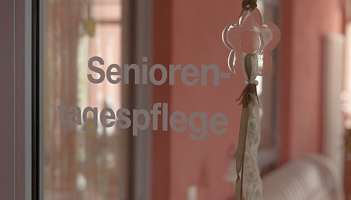 Graue Aufschrift "Seniorentagespflege" auf Glastür 