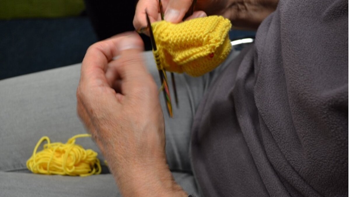Zwei Hände stricken mit gelber Wolle