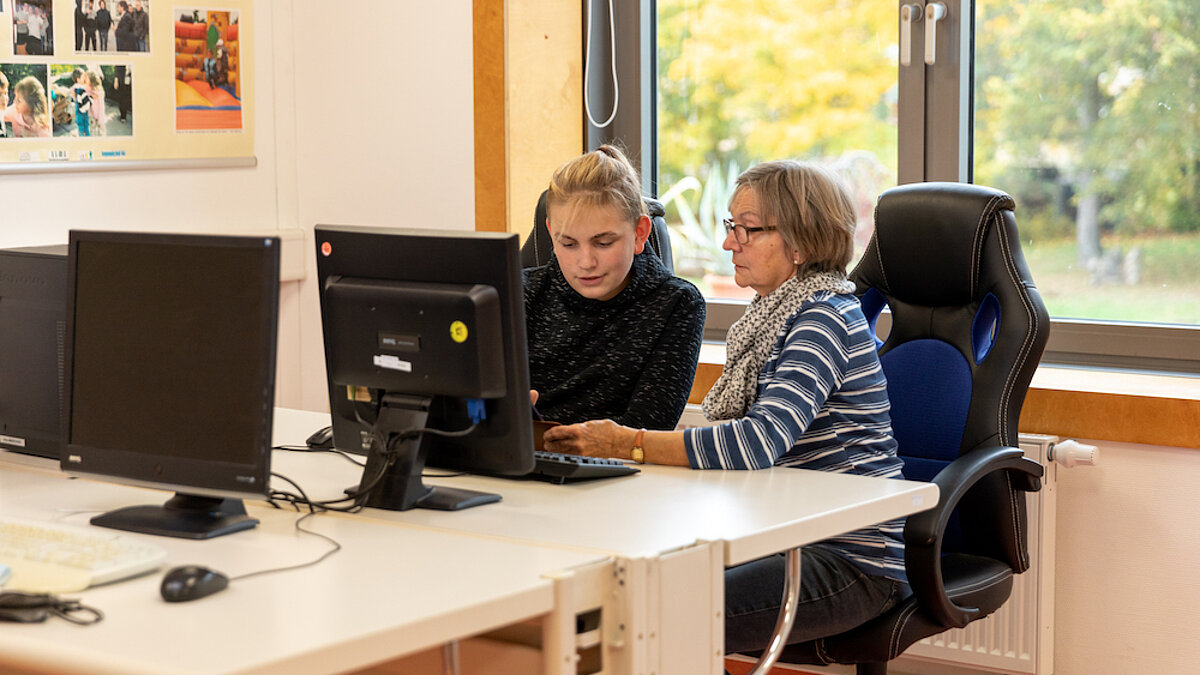 Eine ältere Frau und ein Teenager sitzen am Computer-Bildschirm