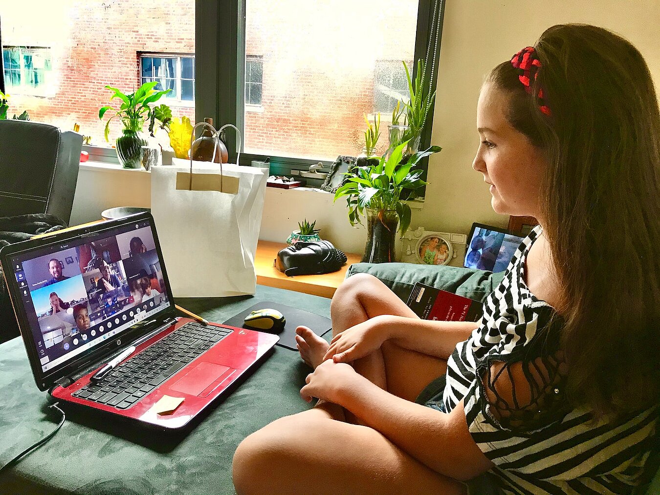 Mädchen sitzt vor Laptop, auf dem eine Videokonferenz läuft
