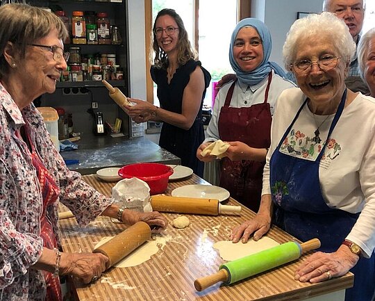 Gruppe von Menschen verschiedenen Alters, die in einer Küche stehen und gemeinsam backen. 