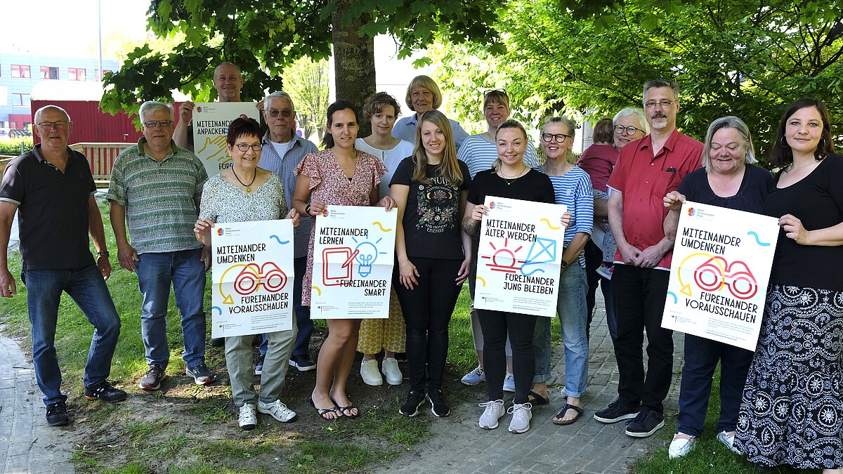 Mehrere Menschen stehen im Garten des Mehrgenerationenhauses und halten Schilder in die Kamera