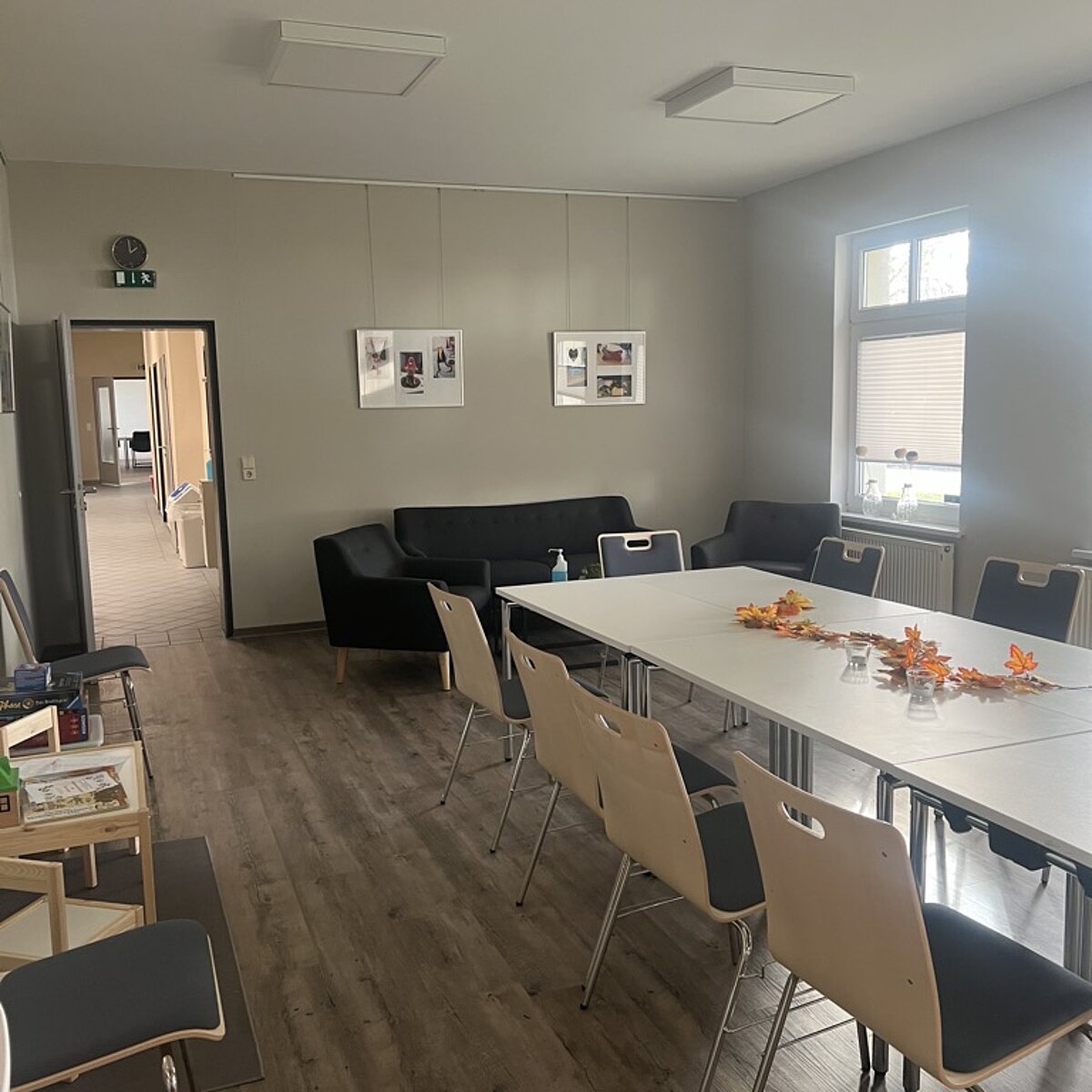 Der Clubraum fotografiert aus der hinteren rechten Ecke. Zu sehen sind eine kleine Lounge-Ecke, der Kinder-Spieltisch und die große Tafel mit Stühlen in der Mitte.