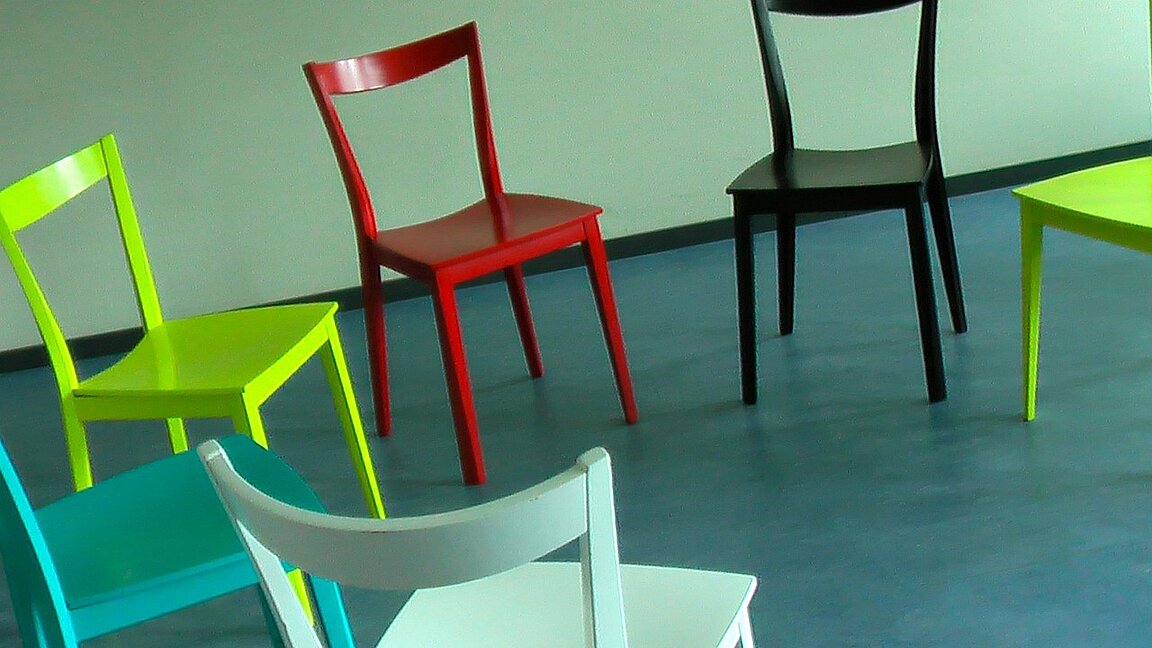 Stuhlkreis mit Holzstühlen in verschiedenen Farben