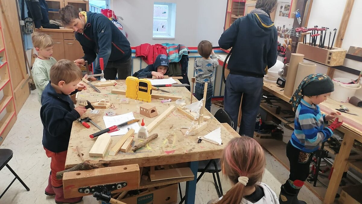 Zwei Eltern und sechs Kinder arbeiten mit Holz in einer Werkstatt