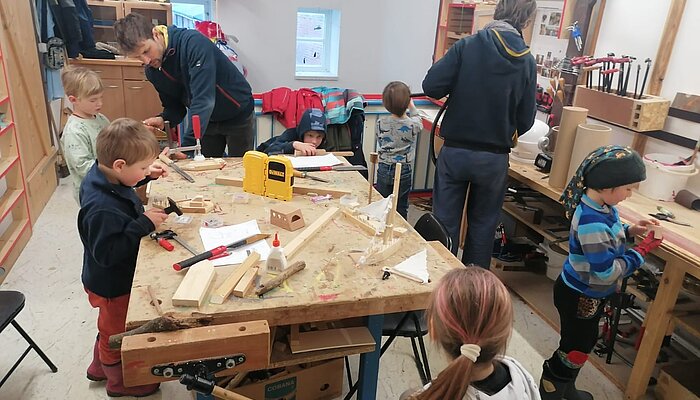 Zwei Eltern und sechs Kinder arbeiten mit Holz in einer Werkstatt