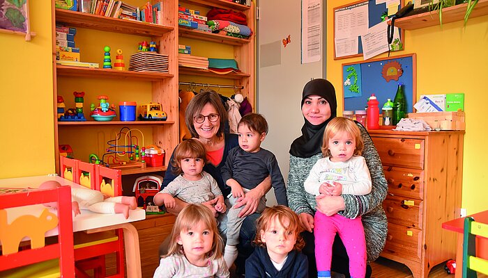 Zwei Frauen sitzen mit fünf Kindern in einem Spielzimmer
