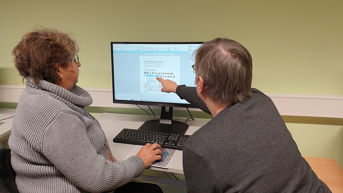 Zwei ältere Damen sitzen vor einem Computerbildschirm.