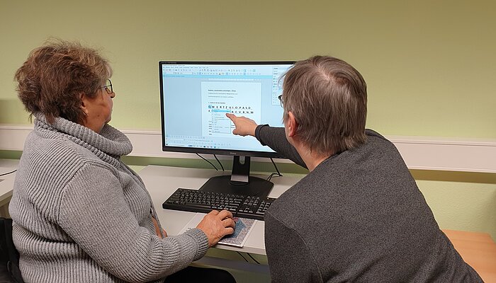 Zwei ältere Damen sitzen vor einem Computerbildschirm.