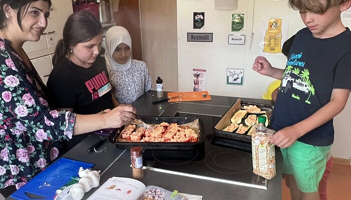 Eine Frau und drei Kinder stehen um eine Kochinsel und legen gefüllte Paprika und Zucchini auf ein Backbleche.