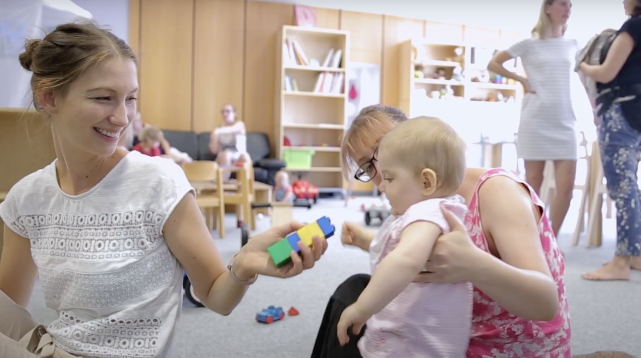 Eine Frau hält ein Baby, eine andere hält ihm Bausteine hin.