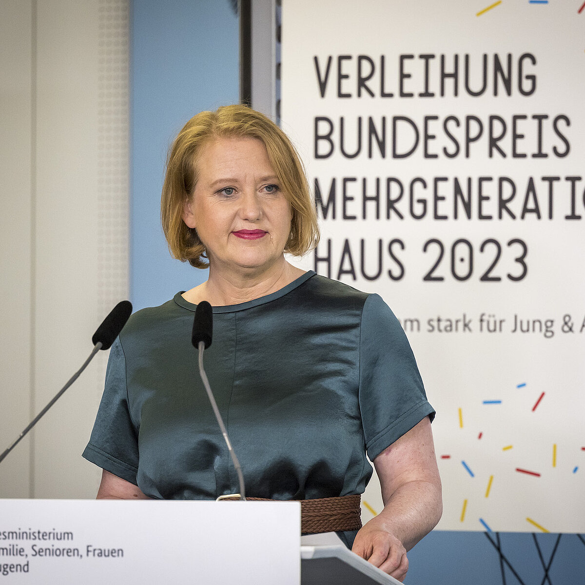 Eine Frau steht an einem Rednerpult und lächelt. 