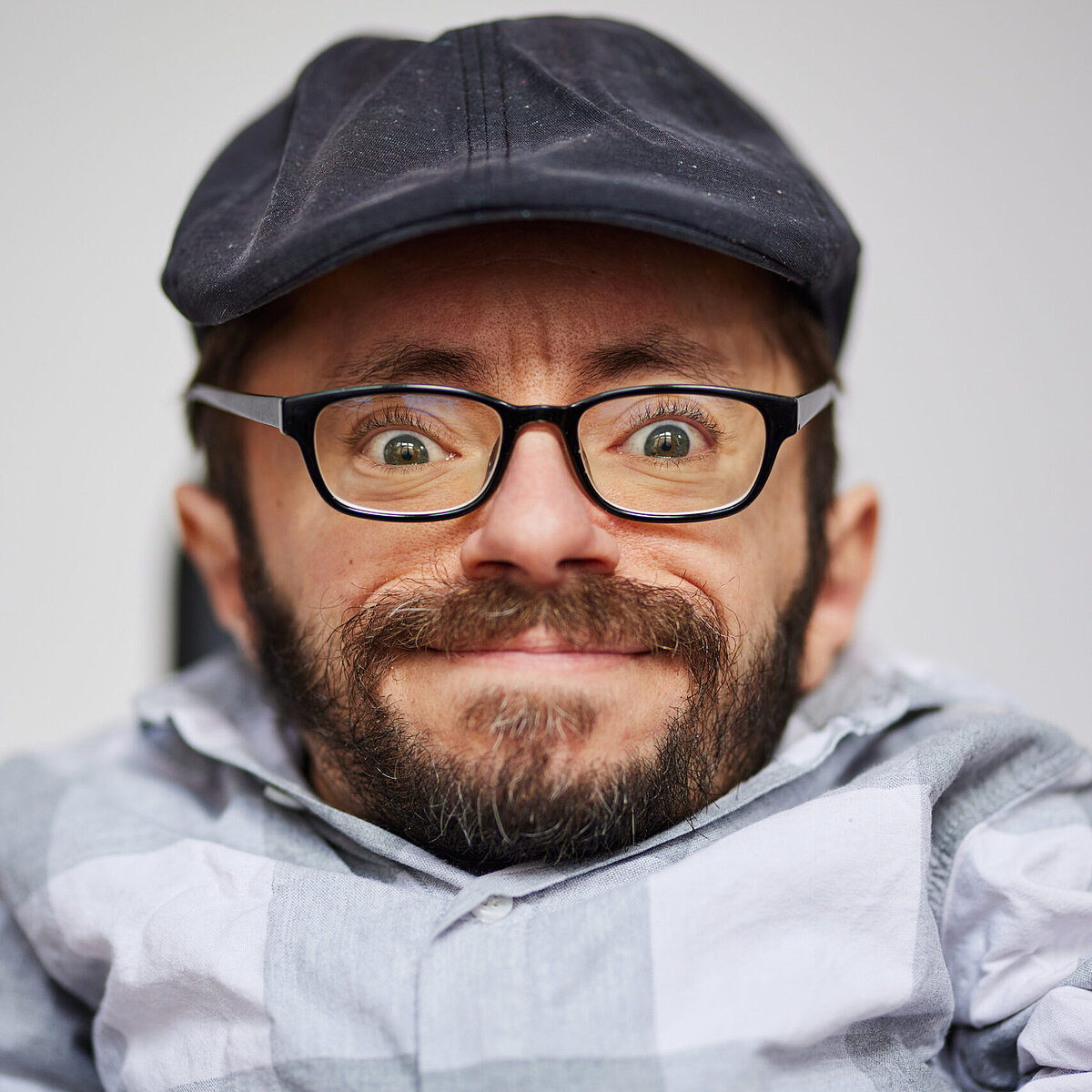 Porträtbild von Raul Krauthausen, er trägt ein graues Hemd, eine dunkle Mütze und Brille