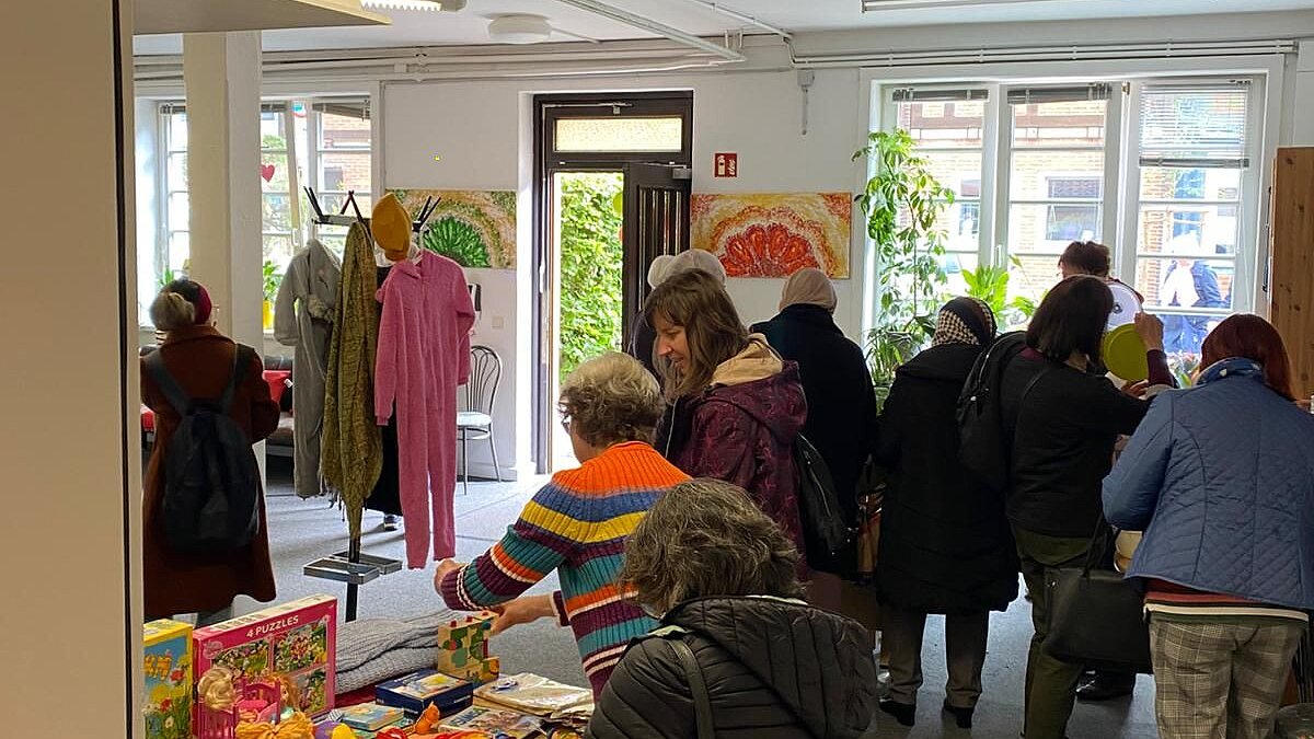 Im Foyer des MGH stehen Tische mit Dingen, die getauscht werden können. Mehrere Personen interessieren sich