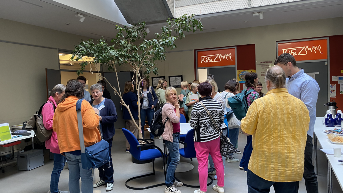 Blick von oben auf viele Menschen, die in einem Foyer stehen und sich in verschiedenen Gruppen unterhalten