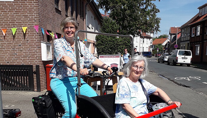 Eine Frau sitzt in einer Fahrrad-Rikscha, die von einer weiteren Frau gefahren wird.