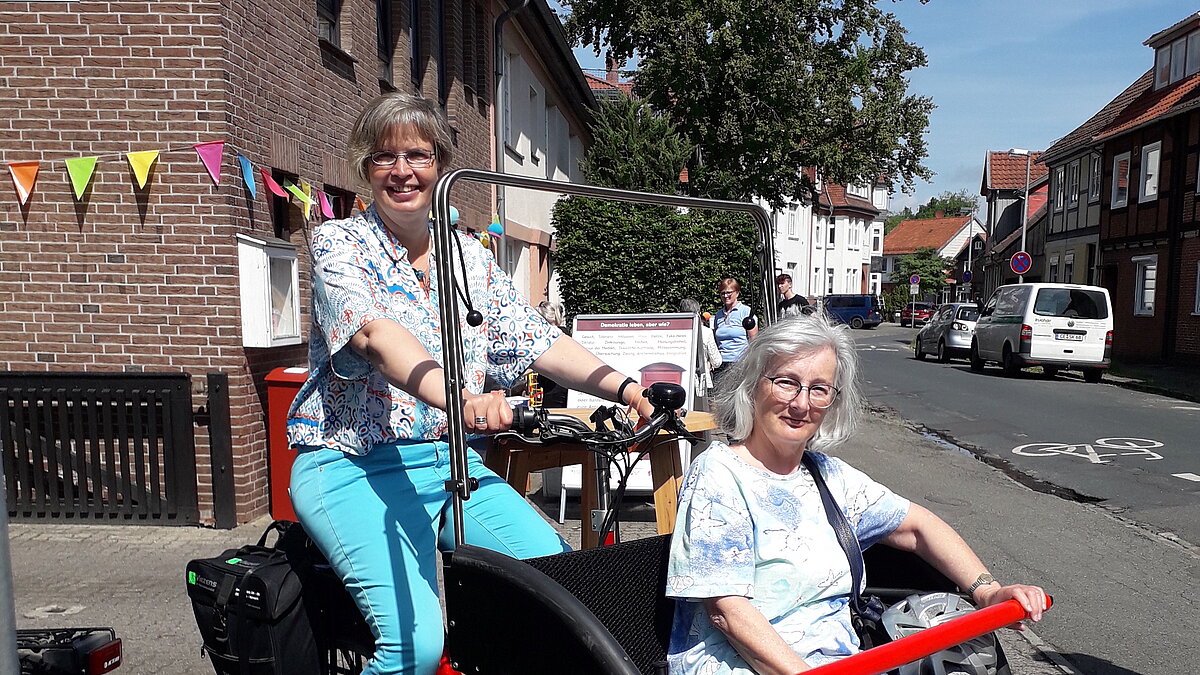 Eine Frau sitzt in einer Fahrrad-Rikscha, die von einer weiteren Frau gefahren wird.