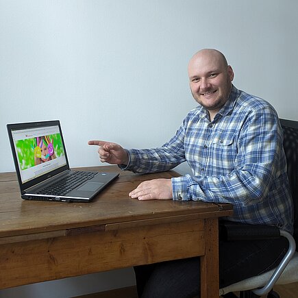 Ein Mann sitzt an einem Tisch und zeigt auf einen Laptop