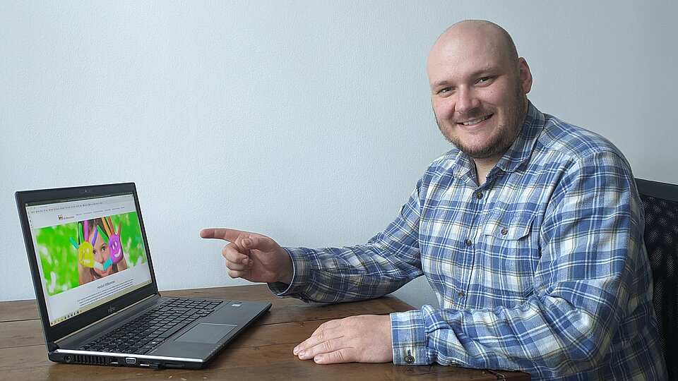 Ein Mann sitzt an einem Tisch und zeigt auf einen Laptop