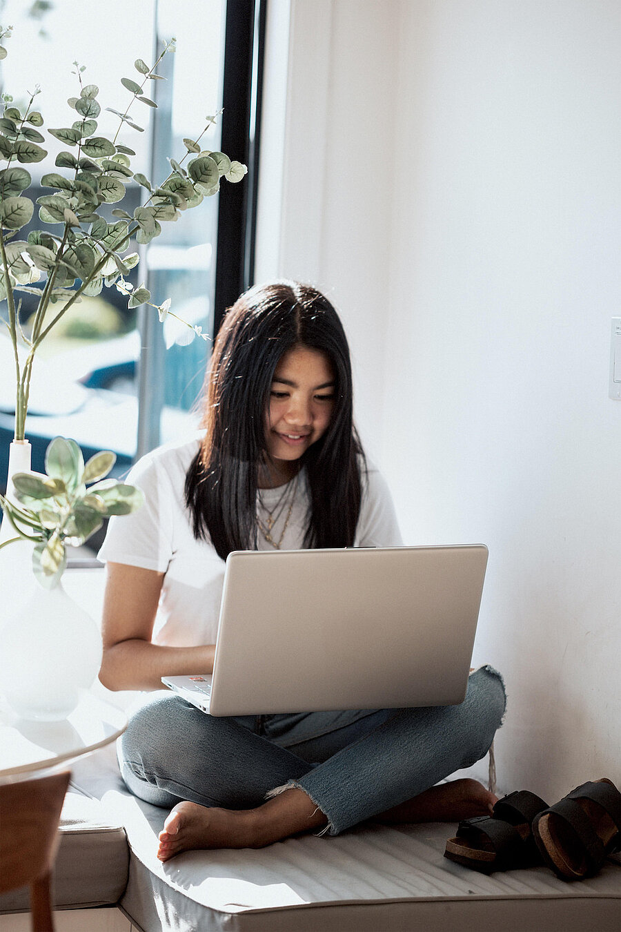 Mädchen sitzt im Schneidersitz mit Laptop auf dem Schoß