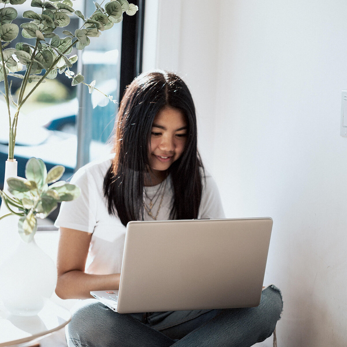 Mädchen sitzt im Schneidersitz mit Laptop auf dem Schoß