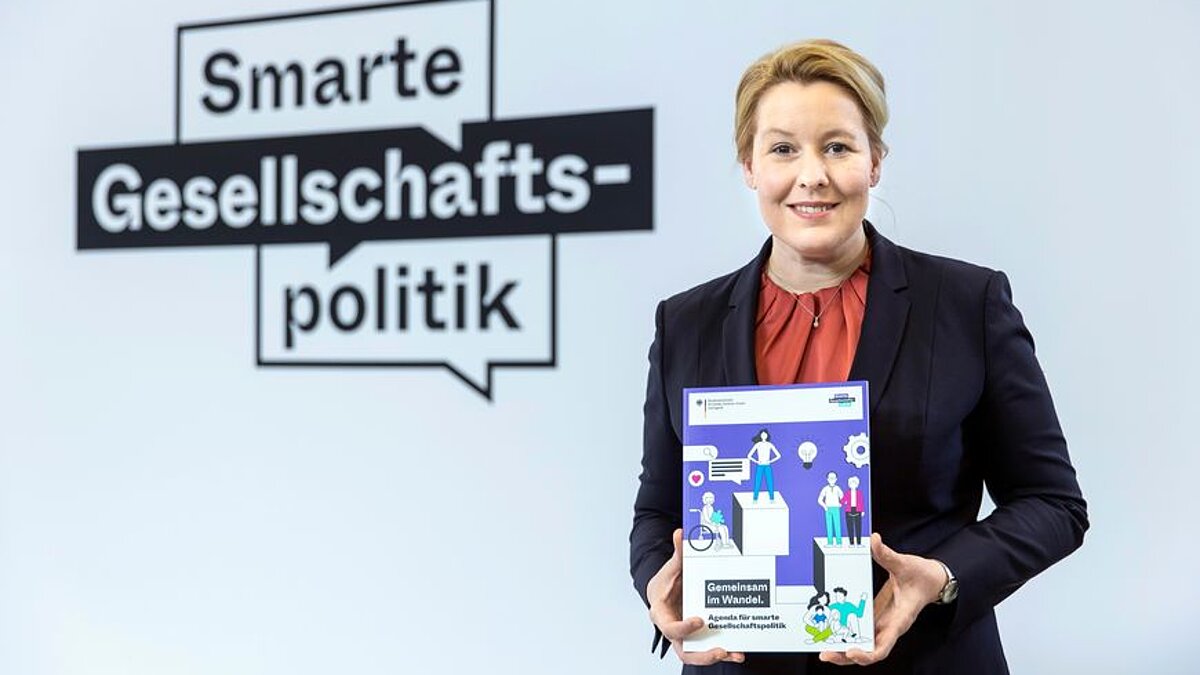 Franziska Giffey hält lächelnd eine Broschüre in die Kamera
