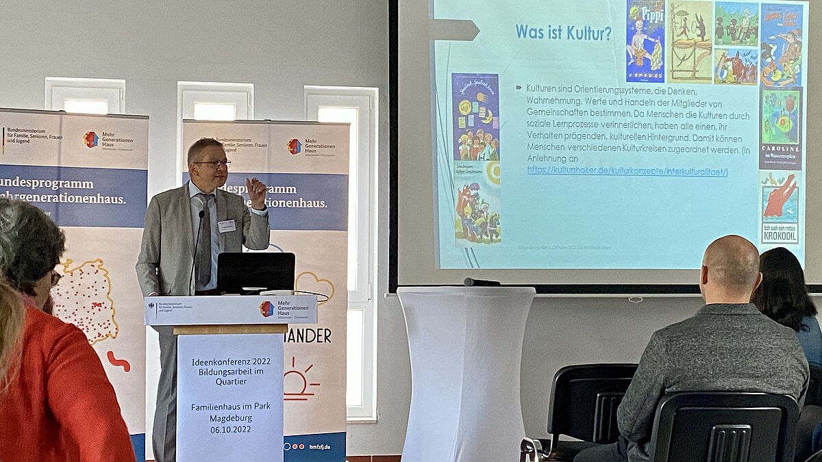 Dr. Winfried Kösters steht an einem Rednerpult vor einer Leinwand mit Präsentation
