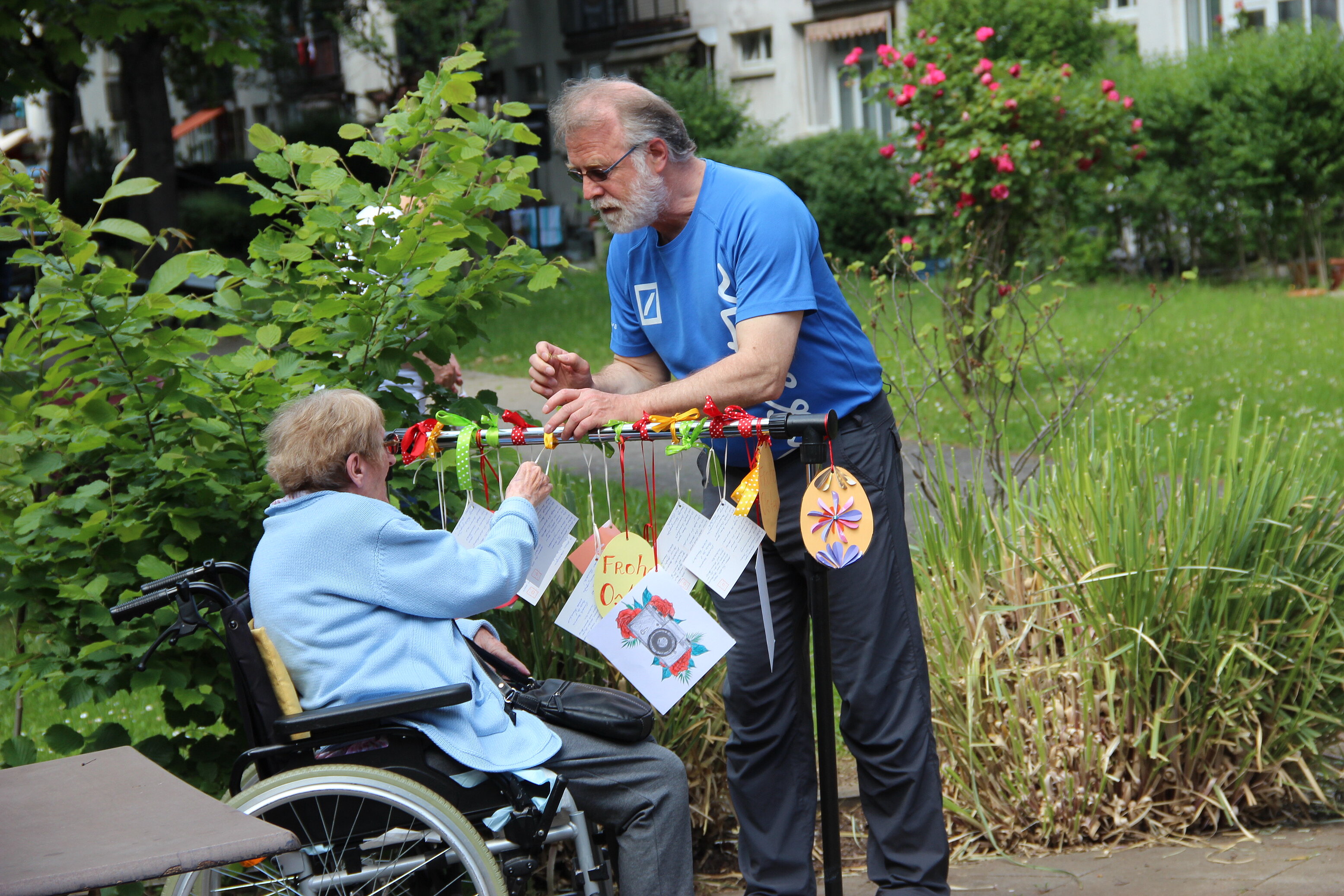 Holger Tümmler hängt mit einer älteren Frau im Rollstuhl Bilder auf.