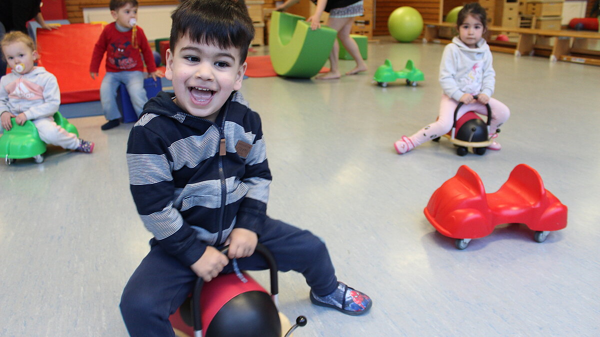 Vier Kinder fahren auf Bobbycars durch eine Turnhalle