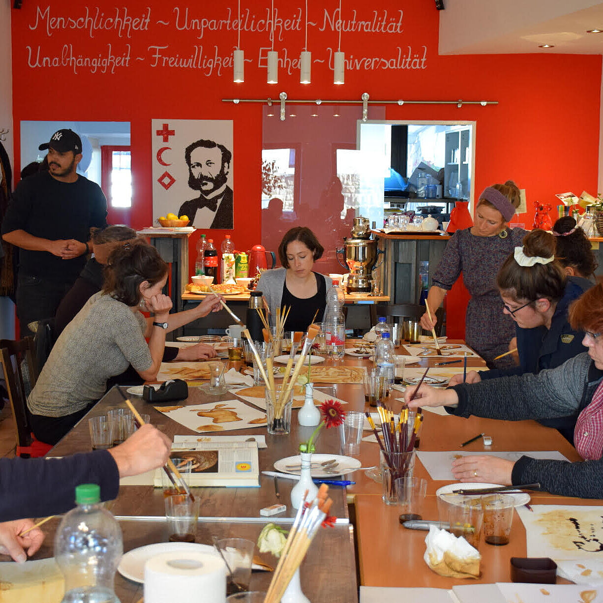 Mehrere Personen sitzen an einem großen Tisch und malen mit Wasserfarbe
