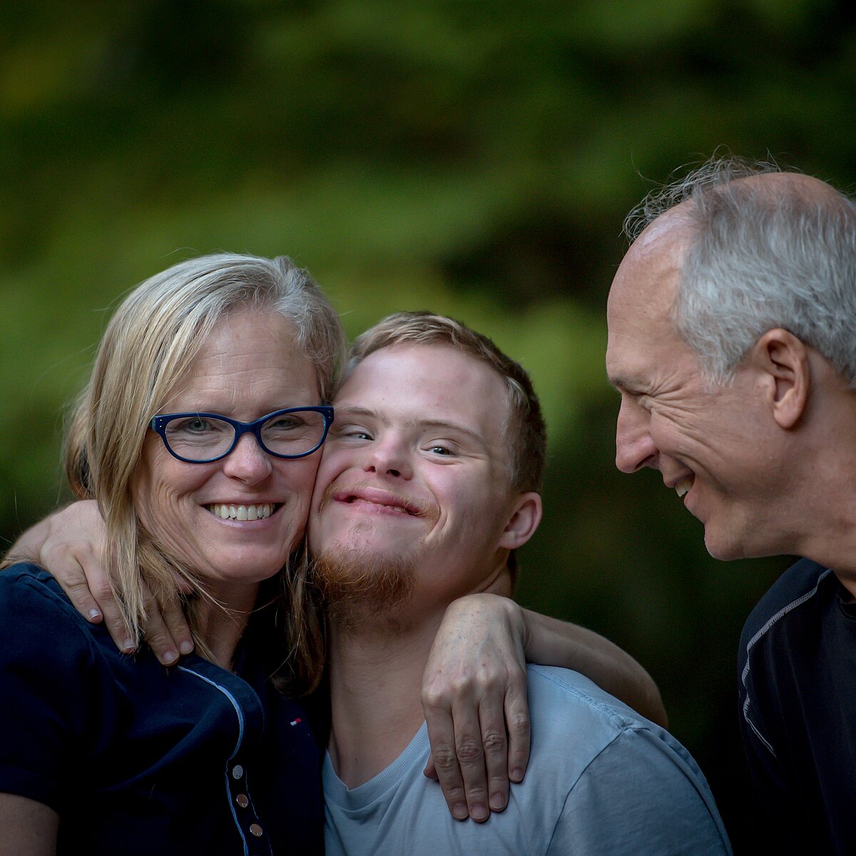 Eine Mutter und ein Vater mit ihrem Sohn in ihrer Mitte, alle drei lächeln. 