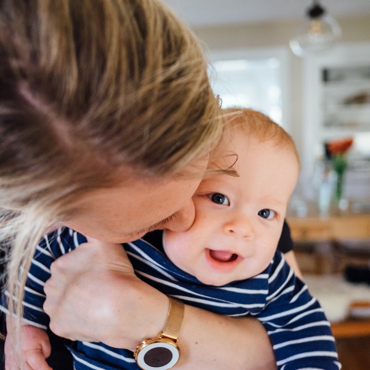 Frau mit blonden Haaren hält Baby auf dem Arm, das in die Kamera schaut