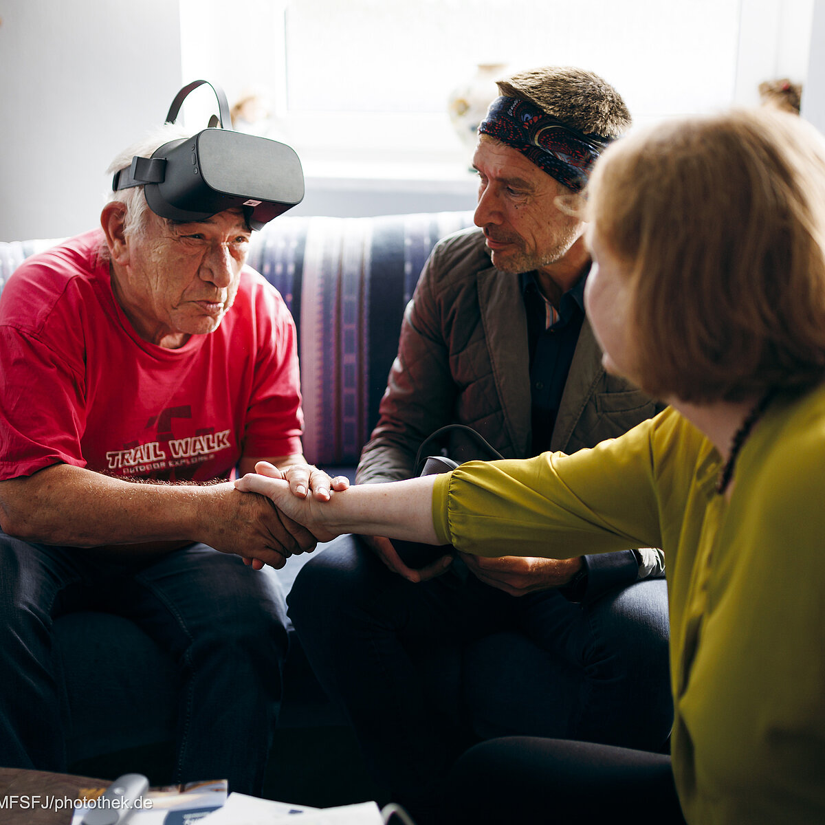 Bundesfamilienministerin Lisa Paus reicht einem älteren Mann, der eine VR-Brille auf der Stirn trägt, die Hand, ein weiterer älterer Herr sitzt daneben.