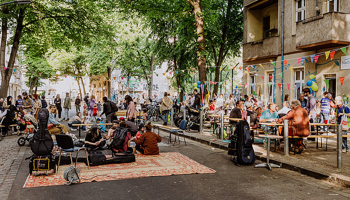 Menschen sitzen an Biertischgarnituren und feiern am "Tag der Nachbarschaft" auf der Mahlower Straße in Berlin.