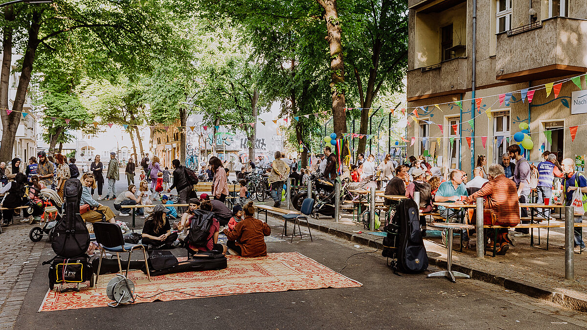 Menschen sitzen an Biertischgarnituren und feiern am "Tag der Nachbarschaft" auf der Mahlower Straße in Berlin.