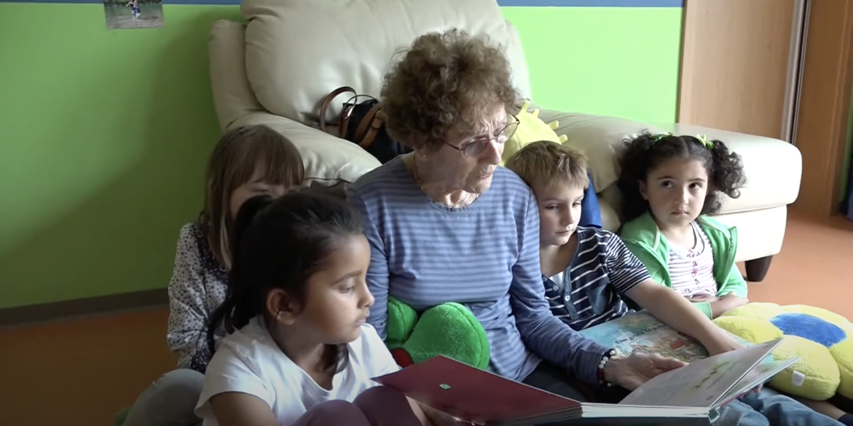 Eine ältere Frau liest vier Kindern aus einem Bilderbuch vor