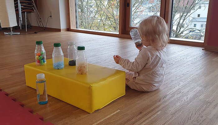Baby sitzt auf dem Boden und spielt mit Flaschen.