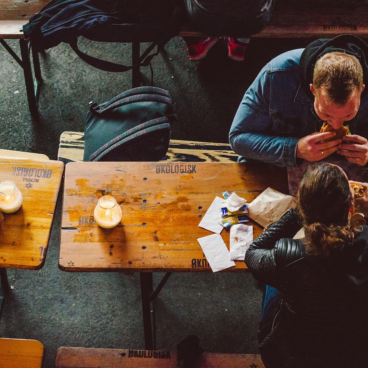 Drei Menschen sitzen an Biertischen und essen, Perspektive von oben auf die Köpfe