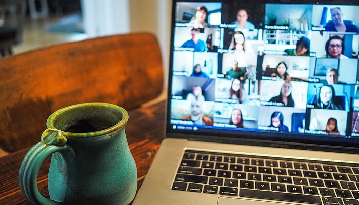 Laptop zeigt verschiedene Menschen in einer Videokonferenz, daneben steht eine Tasse