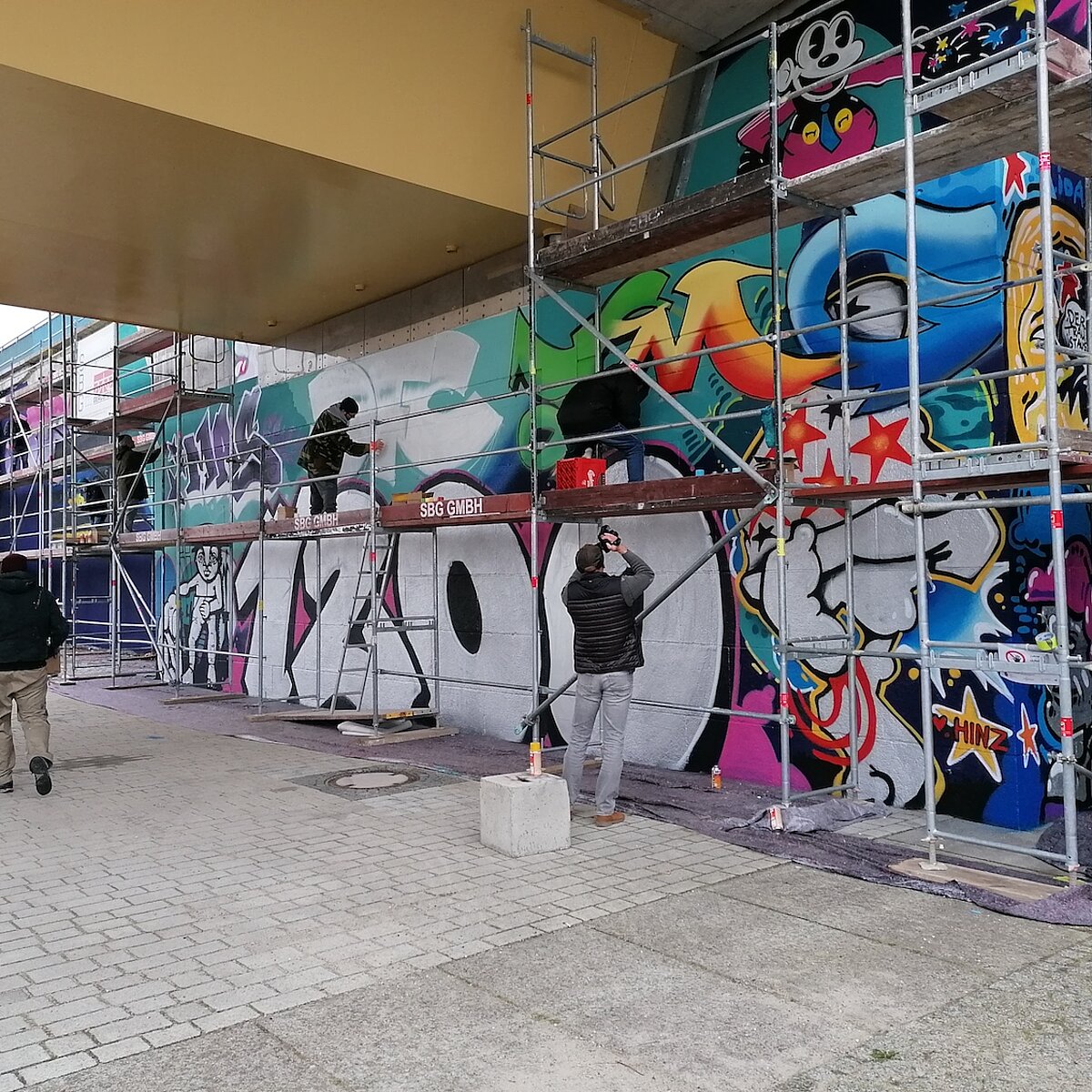 Wand mit Gerüst, auf dem Graffiti-Künstler stehen und sprühen