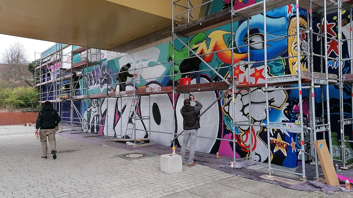 Wand mit Gerüst, auf dem Graffiti-Künstler stehen und sprühen