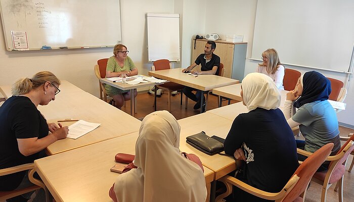 Sechs Frauen und ein Mann sitzen auf Stühlen um einen Tisch