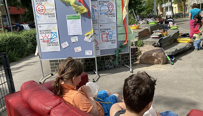 Zwei Metaplanwände stehen in einer Fußgängerzone, Bücher liegen auf einer Steintreppe aus, Kinder sitzen auf einem Sofa und lesen