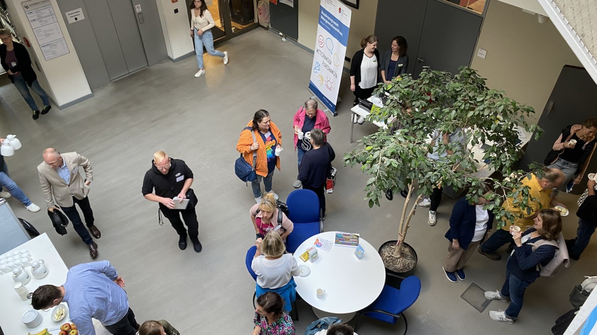 Blick von oben auf zahlreiche Menschen, die in einem Foyer stehen und sich in verschiedenen Gruppen unterhalten