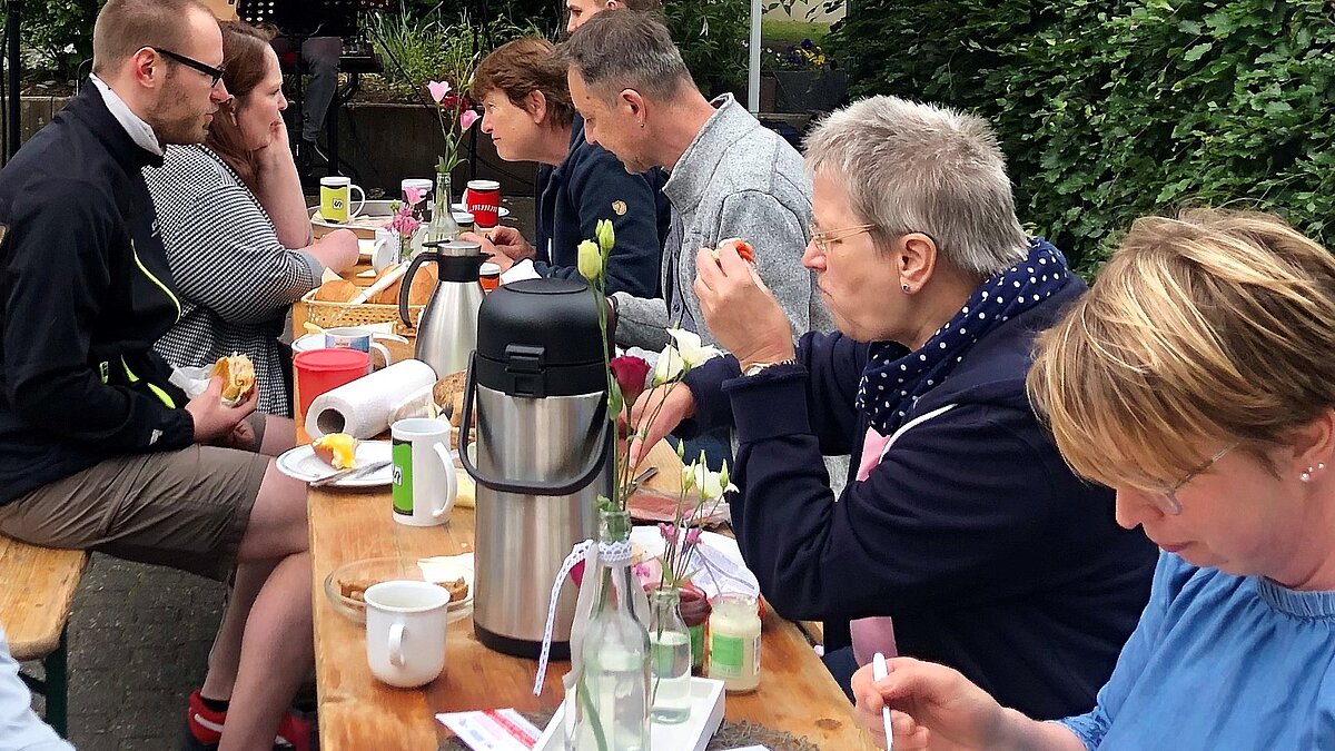 Acht Menschen sitzen an einem Biertisch und frühstücken.
