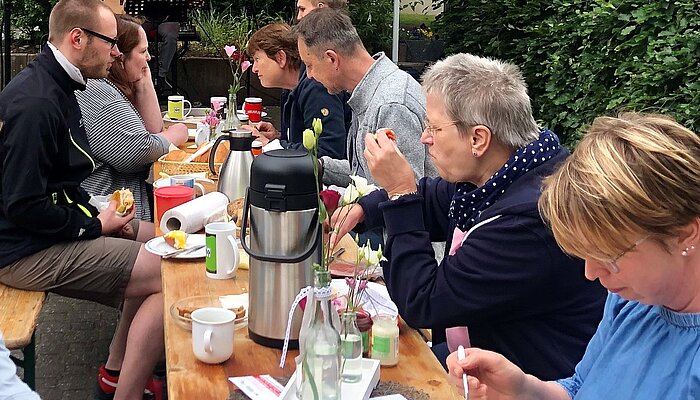 Acht Menschen sitzen an einem Biertisch und frühstücken.