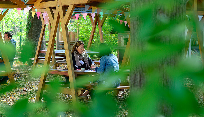 Zwei Frauen sitzen auf einer Holzbank mit Überdachung im Gespräch im Außenbereich des Veranstaltungsortes