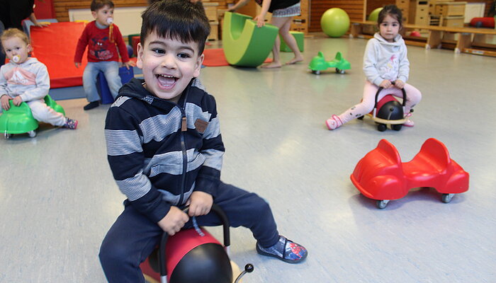 Vier Kinder fahren auf Bobbycars durch eine Turnhalle